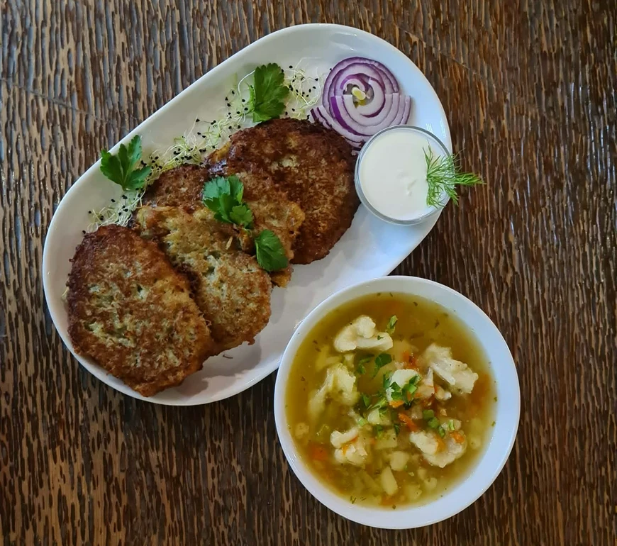 Talerz z&nbsp;kotletami podanymi z&nbsp;czerwoną cebulą, zieleniną i&nbsp;sosem śmietanowym&nbsp;obok miski z&nbsp;zupą jarzynową z&nbsp;kalafiorem