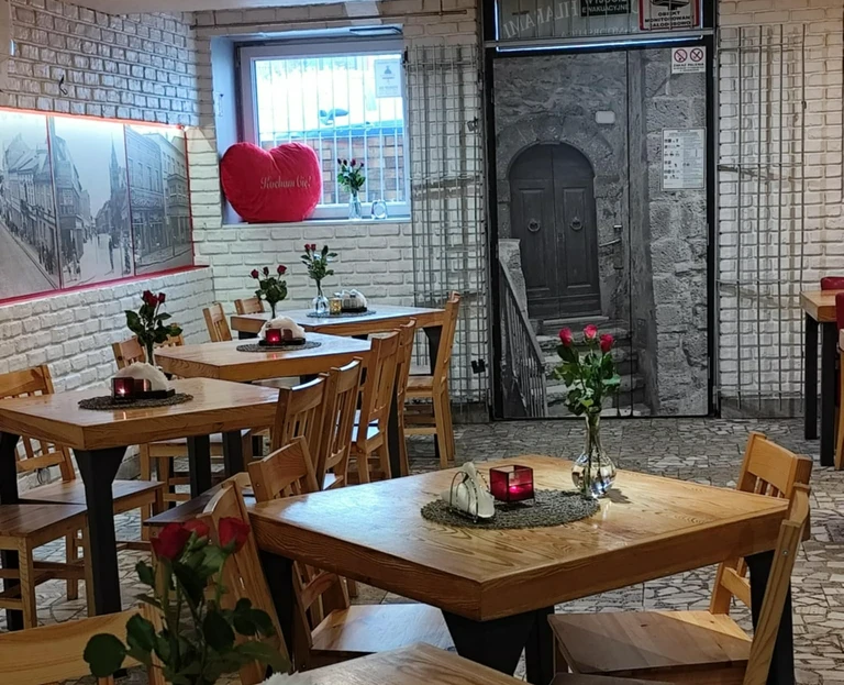 Wnętrze przytulnej restauracji z&nbsp;drewnianymi stolikami, pojedynczymi różami w&nbsp;wazonach i&nbsp;dekoracjami na&nbsp;białych ceglanych ścianach