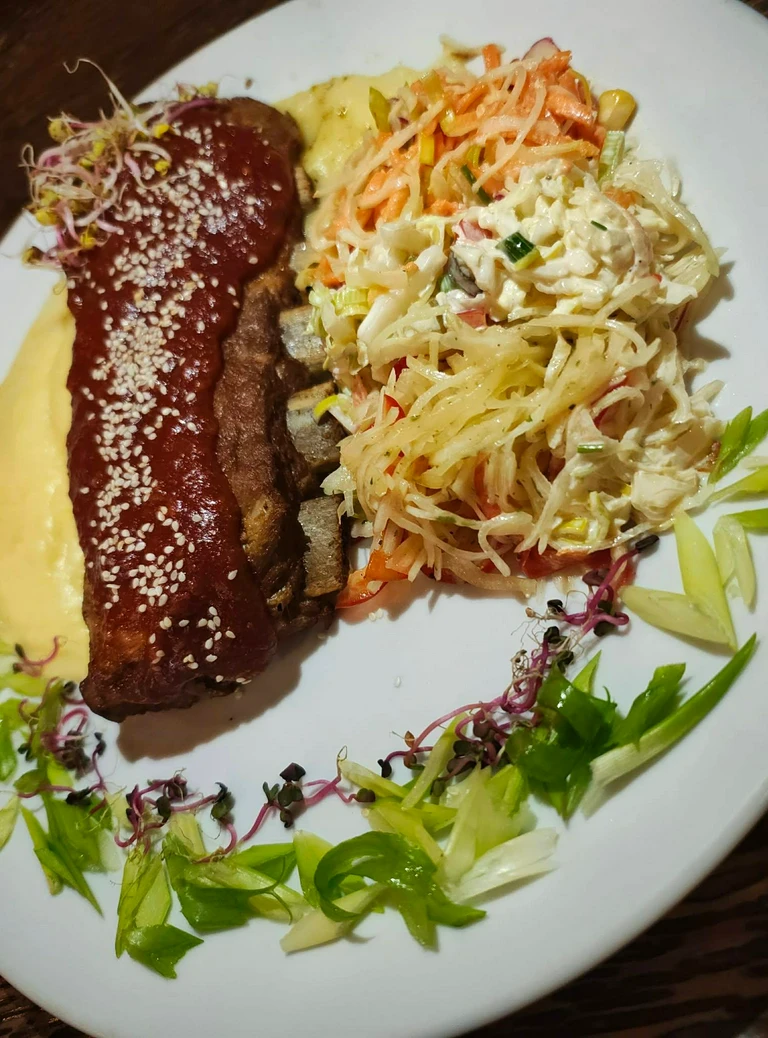 Danie z&nbsp;grillowanym mięsem polanym sosem i&nbsp;posypanym sezamem, podane z&nbsp;kolorową surówką i&nbsp;dekoracją z&nbsp;zielonych liści na&nbsp;białym talerzu