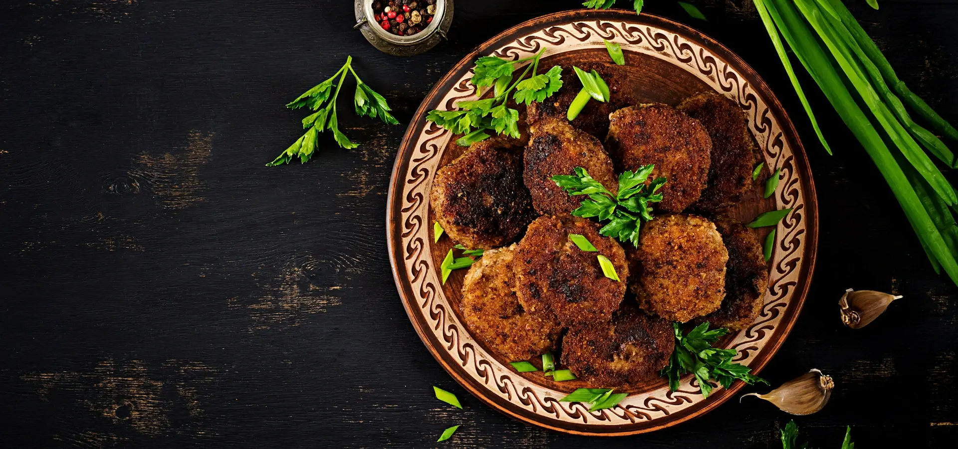 Talerz smażonych kotletów mielonych podanych z&nbsp;natką pietruszki i&nbsp;szczypiorem na&nbsp;ciemnym drewnianym tle